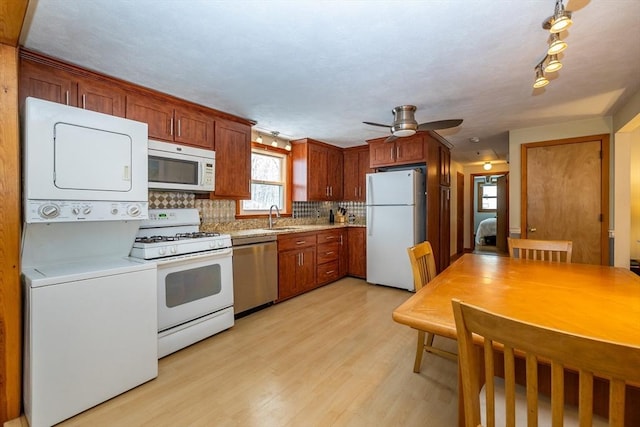 kitchen featuring stacked washer / dryer, sink, light wood-type flooring, backsplash, and white appliances