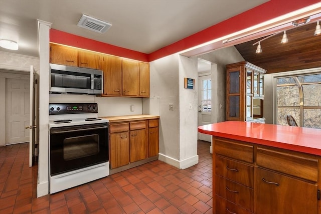 kitchen with visible vents, electric range oven, stainless steel microwave, brick floor, and light countertops