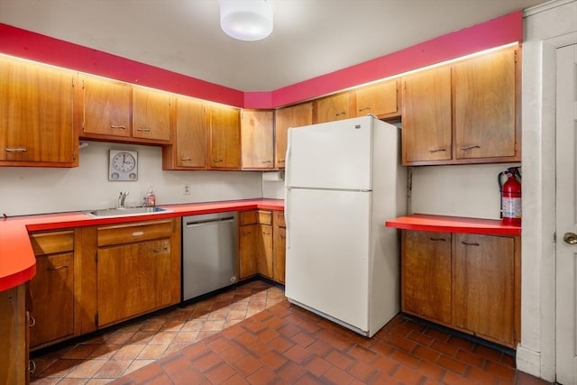 kitchen featuring brown cabinetry, freestanding refrigerator, a sink, and stainless steel dishwasher