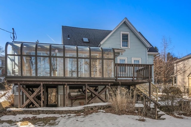 snow covered back of property featuring a deck, a sunroom, a shingled roof, and stairway