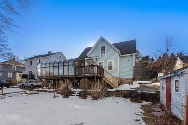 snow covered back of property featuring a deck, a sunroom, and stairway