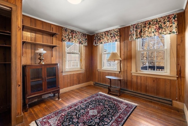 sitting room with a baseboard radiator, wooden walls, baseboards, and hardwood / wood-style floors