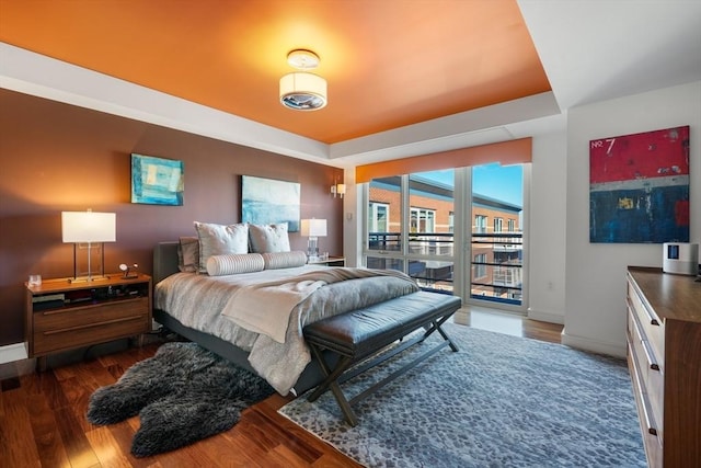 bedroom featuring a tray ceiling, dark hardwood / wood-style floors, and access to outside