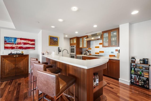 kitchen featuring a kitchen bar, wall chimney range hood, stainless steel appliances, tasteful backsplash, and kitchen peninsula