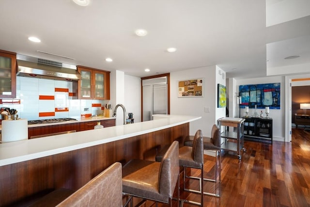 kitchen with kitchen peninsula, backsplash, range hood, and dark hardwood / wood-style floors