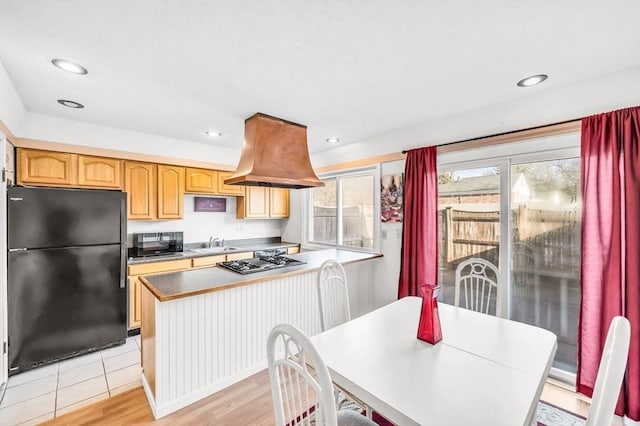 kitchen featuring custom range hood, sink, light hardwood / wood-style floors, and black appliances