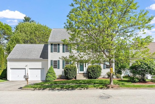 colonial house featuring a garage, driveway, a shingled roof, and a front lawn