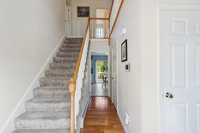 staircase featuring wood finished floors, baseboard heating, and baseboards