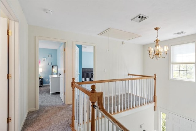 hall featuring attic access, an upstairs landing, light carpet, baseboards, and a chandelier