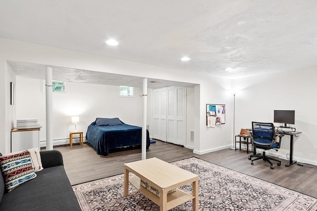 bedroom featuring baseboard heating, wood finished floors, baseboards, recessed lighting, and a desk