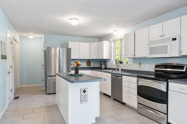 kitchen with stainless steel appliances, a sink, dark countertops, and a center island