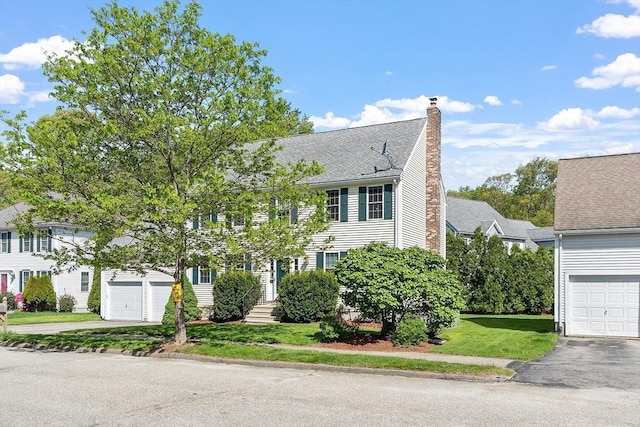 colonial house with a chimney, a front lawn, driveway, and a garage