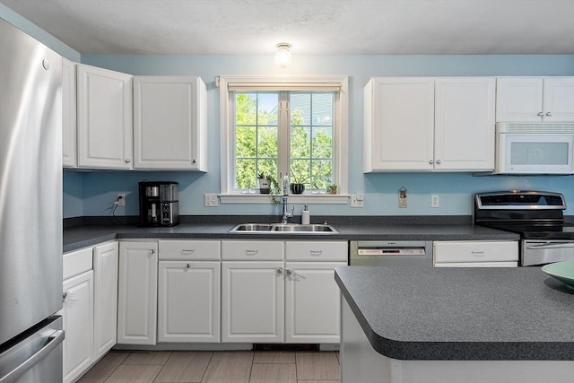kitchen featuring stainless steel appliances, a sink, dark countertops, and white cabinets