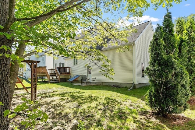 rear view of property with a playground, a yard, a wooden deck, and a shingled roof