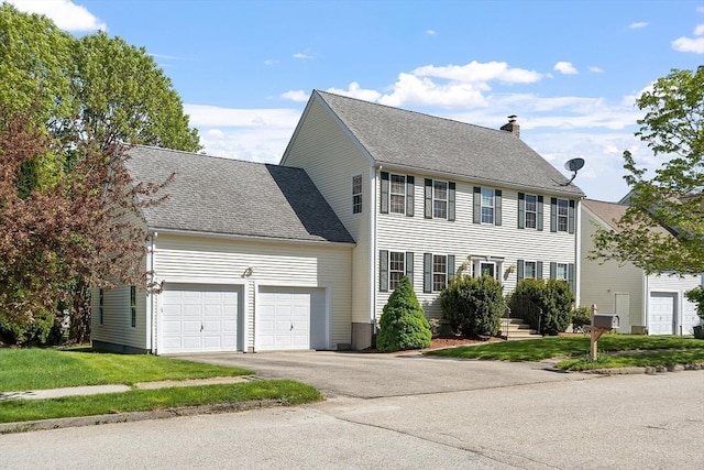 colonial home with a chimney, an attached garage, asphalt driveway, a front yard, and a shingled roof