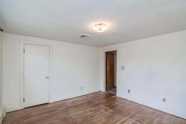 spare room with visible vents, baseboard heating, wood finished floors, and baseboards