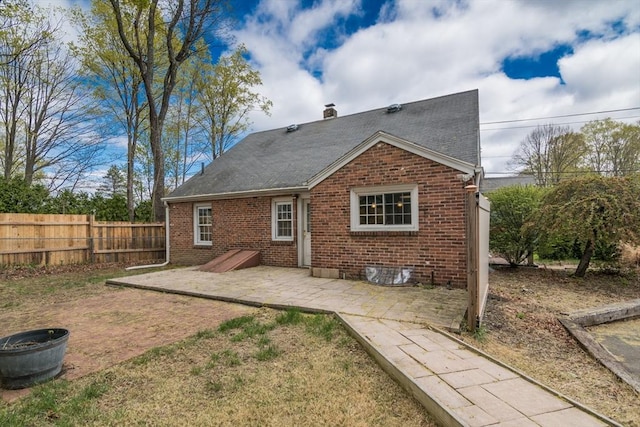 back of property featuring a shingled roof, a patio area, a chimney, brick siding, and fence