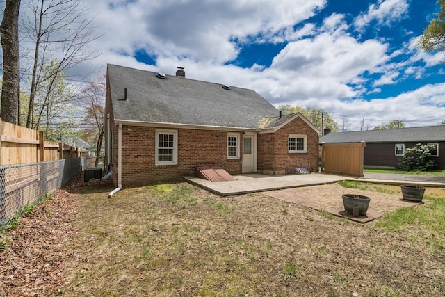 rear view of house featuring a chimney, brick siding, fence, and a patio area