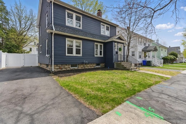 view of front of home featuring a chimney, a front yard, a gate, fence, and aphalt driveway