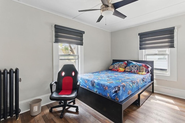 bedroom featuring crown molding, ceiling fan, radiator heating unit, hardwood / wood-style floors, and baseboards