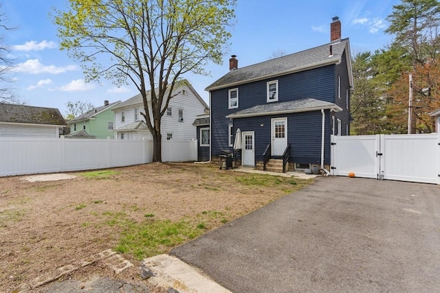 back of house with a chimney, a gate, fence, aphalt driveway, and entry steps