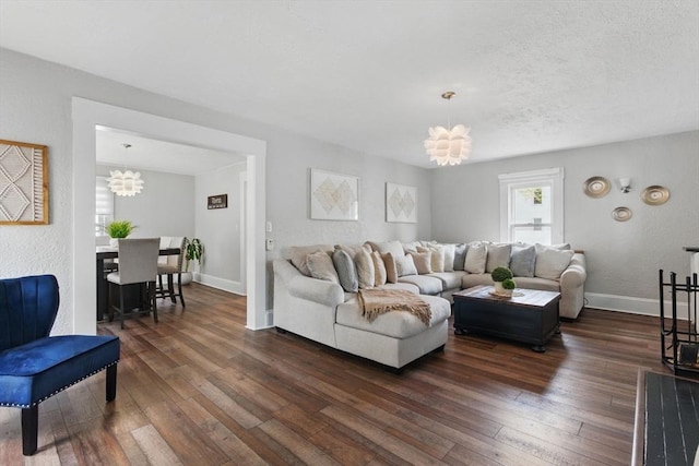 living area with baseboards, a textured wall, dark wood finished floors, and a chandelier