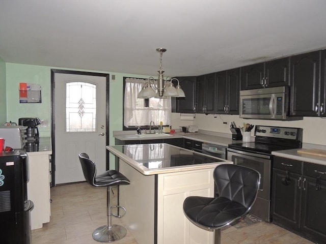 kitchen with appliances with stainless steel finishes, a breakfast bar, sink, an inviting chandelier, and a center island