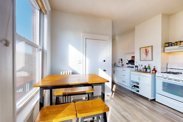 kitchen featuring sink, white gas range, white cabinetry, exhaust hood, and light hardwood / wood-style floors