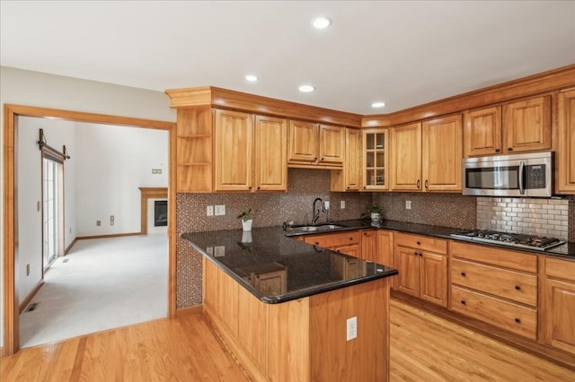 kitchen with tasteful backsplash, kitchen peninsula, appliances with stainless steel finishes, light carpet, and sink