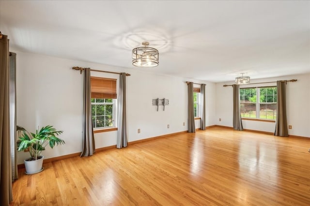 empty room featuring a healthy amount of sunlight, light hardwood / wood-style flooring, and an inviting chandelier