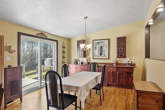 dining space with light hardwood / wood-style floors, vaulted ceiling, a textured ceiling, and an inviting chandelier