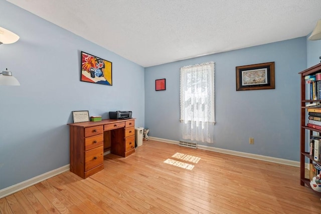 home office featuring baseboards, a textured ceiling, visible vents, and light wood-style flooring