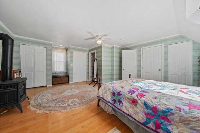 bedroom featuring wallpapered walls, wood finished floors, ornamental molding, two closets, and a wood stove