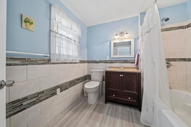 bathroom with a wainscoted wall, shower / bathtub combination with curtain, toilet, vanity, and tile walls