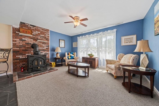 living room with baseboards, a ceiling fan, a wood stove, and visible vents