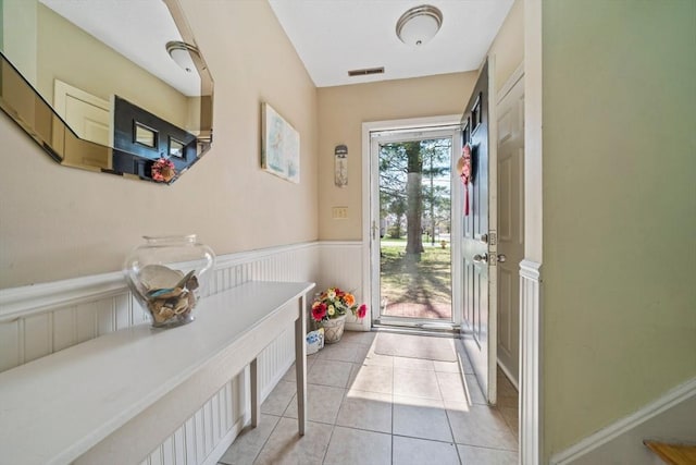doorway featuring a wainscoted wall, visible vents, and light tile patterned floors