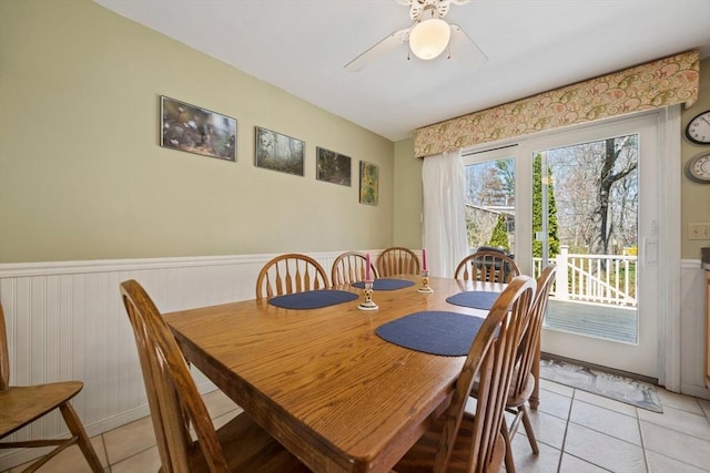 dining area with a wainscoted wall, ceiling fan, and light tile patterned floors