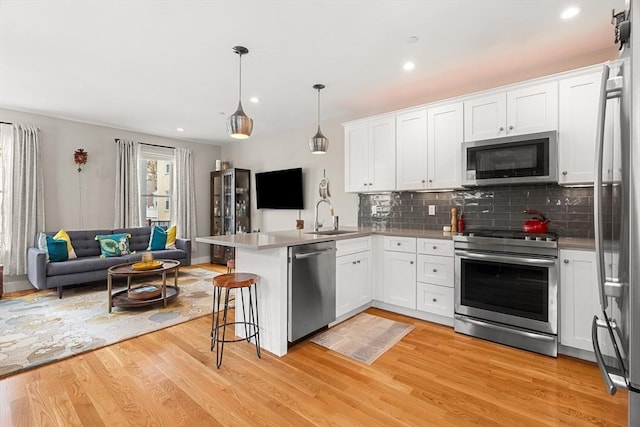 kitchen featuring a sink, a peninsula, open floor plan, stainless steel appliances, and white cabinets