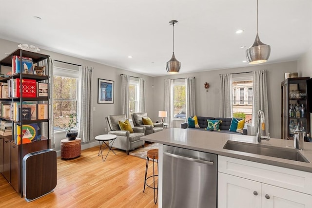 kitchen featuring a sink, stainless steel dishwasher, light wood-style flooring, and open floor plan