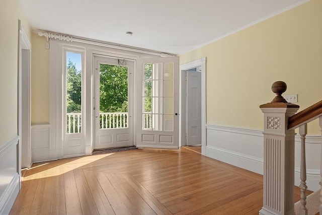 doorway to outside with wainscoting, stairway, a decorative wall, and crown molding