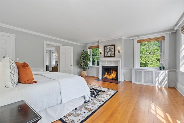 bedroom with multiple windows, a fireplace with flush hearth, hardwood / wood-style flooring, crown molding, and radiator