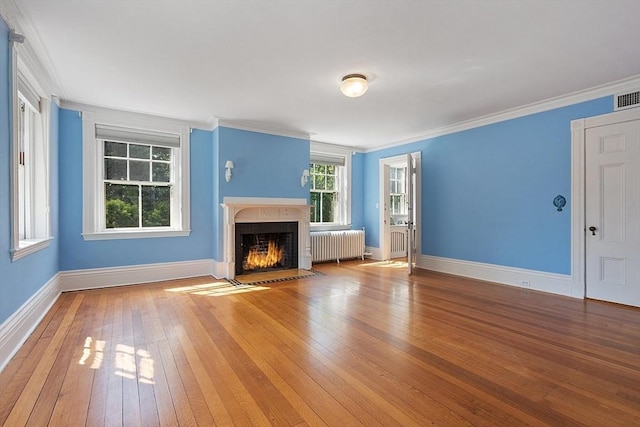 unfurnished living room with radiator heating unit, wood-type flooring, crown molding, a fireplace with flush hearth, and baseboards