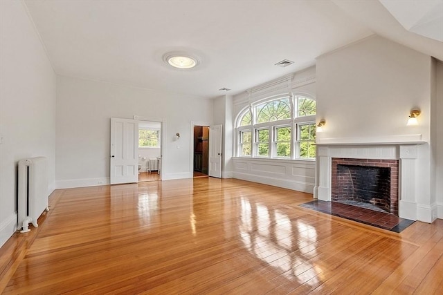 unfurnished living room featuring radiator, hardwood / wood-style flooring, and a brick fireplace