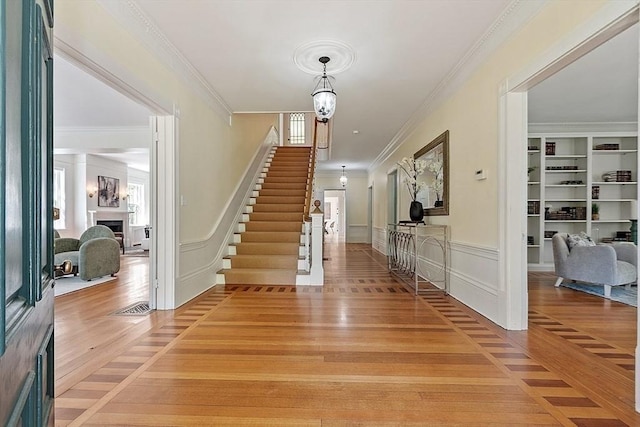 foyer entrance featuring stairs, a fireplace, light wood-style flooring, crown molding, and a decorative wall