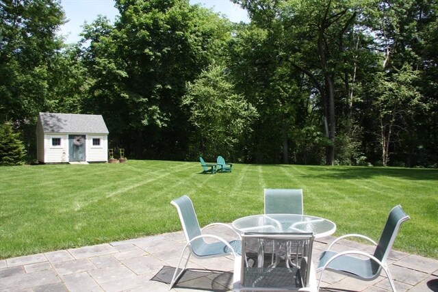 view of green lawn with a patio, an outdoor structure, a storage unit, and outdoor dining space
