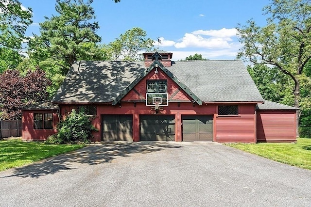 view of front of house with roof with shingles, a detached garage, asphalt driveway, and a front lawn