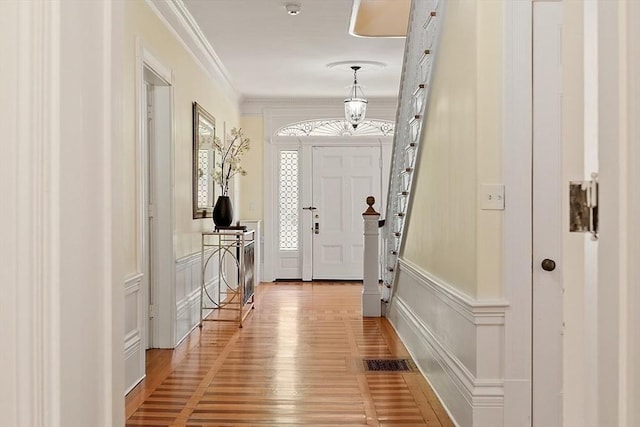 foyer entrance with crown molding, light wood-type flooring, a decorative wall, and wainscoting