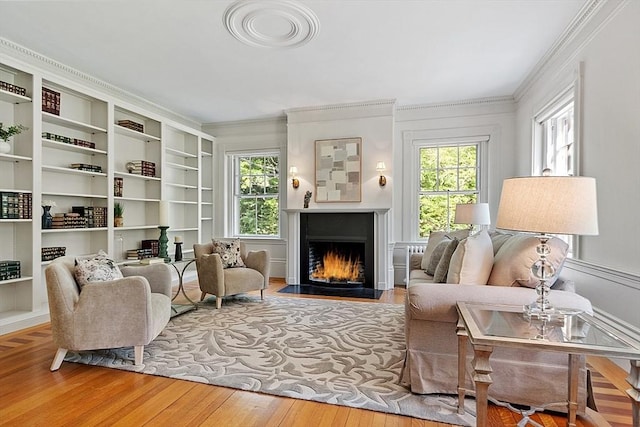 sitting room featuring healthy amount of natural light, ornamental molding, wood finished floors, and a fireplace with flush hearth