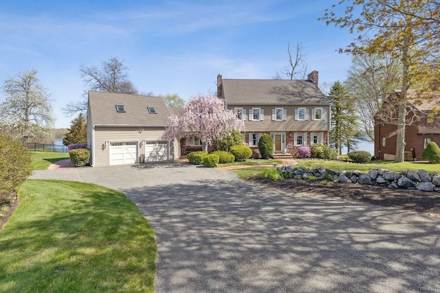 colonial house featuring driveway, a chimney, a front yard, and a garage