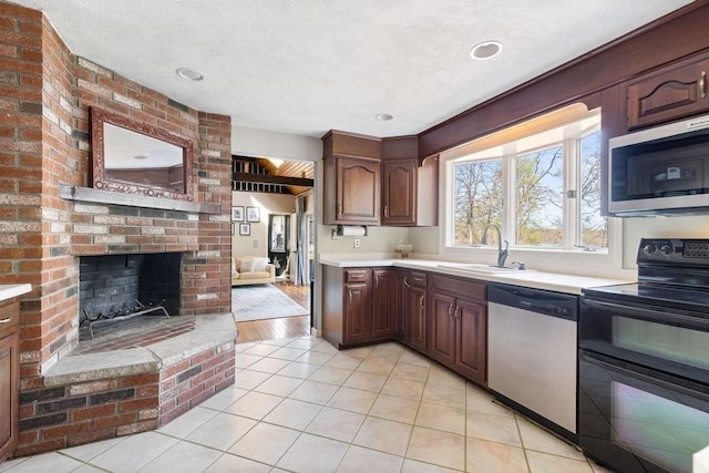 kitchen with light tile patterned flooring, appliances with stainless steel finishes, a sink, a fireplace, and light countertops